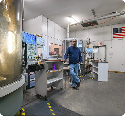 Machinist standing beside CNC machinery inside a precision manufacturing facility